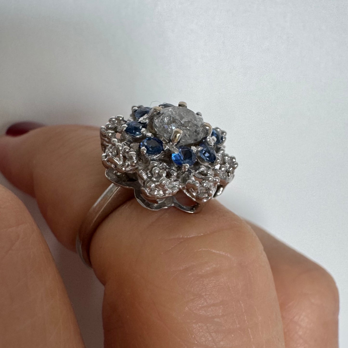 18K gold ring featuring a large round Diamond at the center, surrounded by a floral halo of purple -blue Tanzanite and & Diamonds.