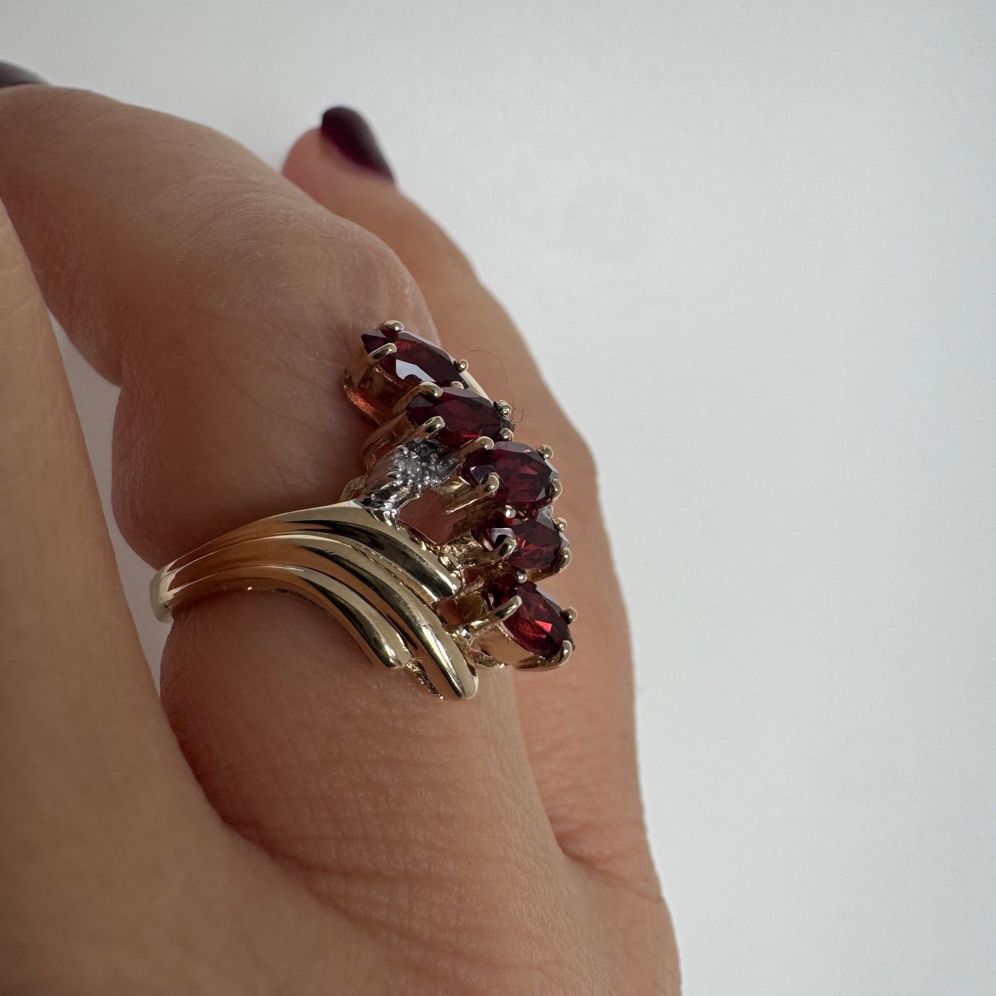 טבעת זהב צהוב 10 קראט בעיצוב דינמי ומלא תנועה, משובצת אבני גרנט בחיתוך מרקיזה בגוון אדום עמוק ובמרכזה נגיעות יהלומים לבנים.
