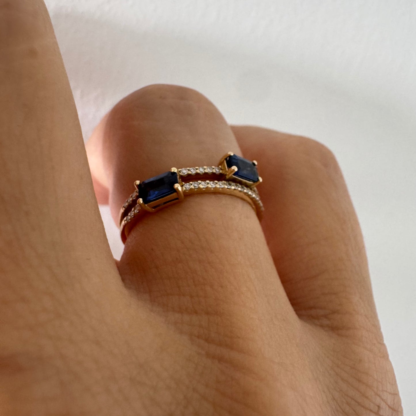 טבעת זהב צהוב 14 קראט בעיצוב פתוח, משובצת שתי אבני ספיר בחיתוך אמרלד ושורות יהלומים עדינים.