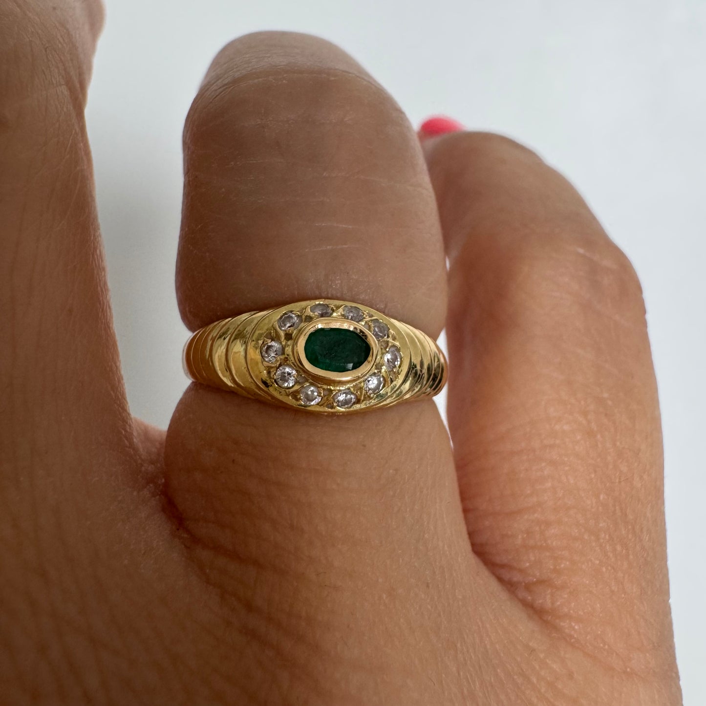 18K gold ring set with an oval Emerald at the center surrounded by Diamonds