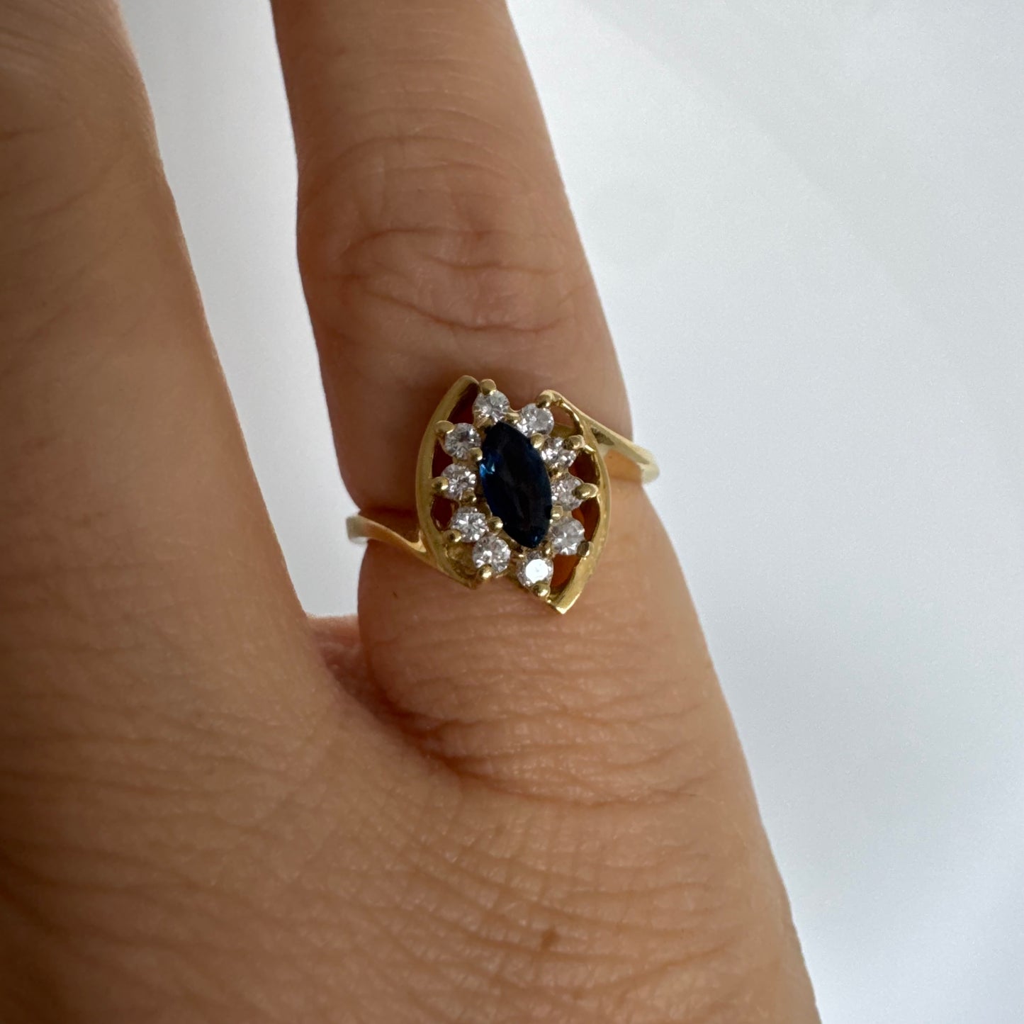 טבעת זהב צהוב 18 קראט משובצת ספיר כחול מרכזי בחיתוך מרקיזה, מוקף הילה של יהלומים המעניקים ניצוץ עדין ומדגישים את צבע האבן העמוק.