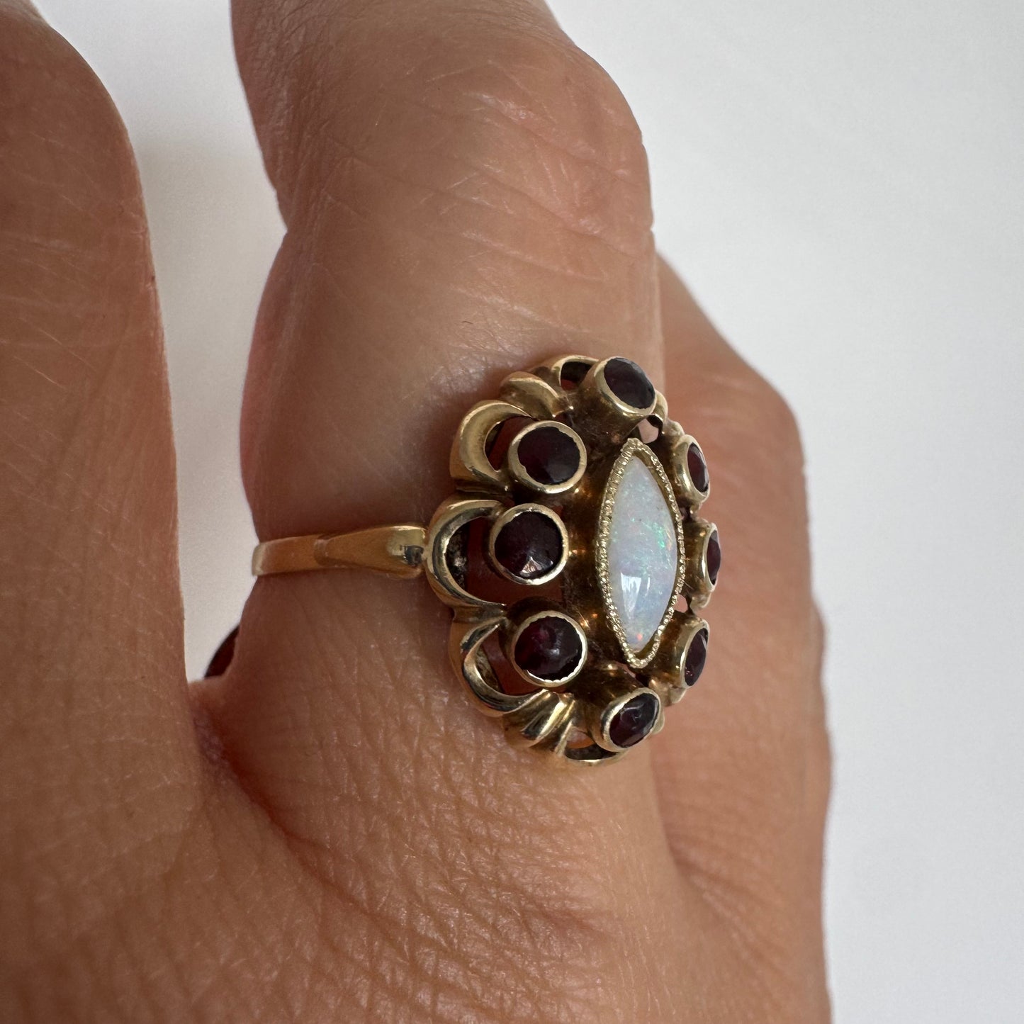 14K gold ring set with a luminous marquise-cut Opal at the center, surrounded by deep red Garnet cabochons