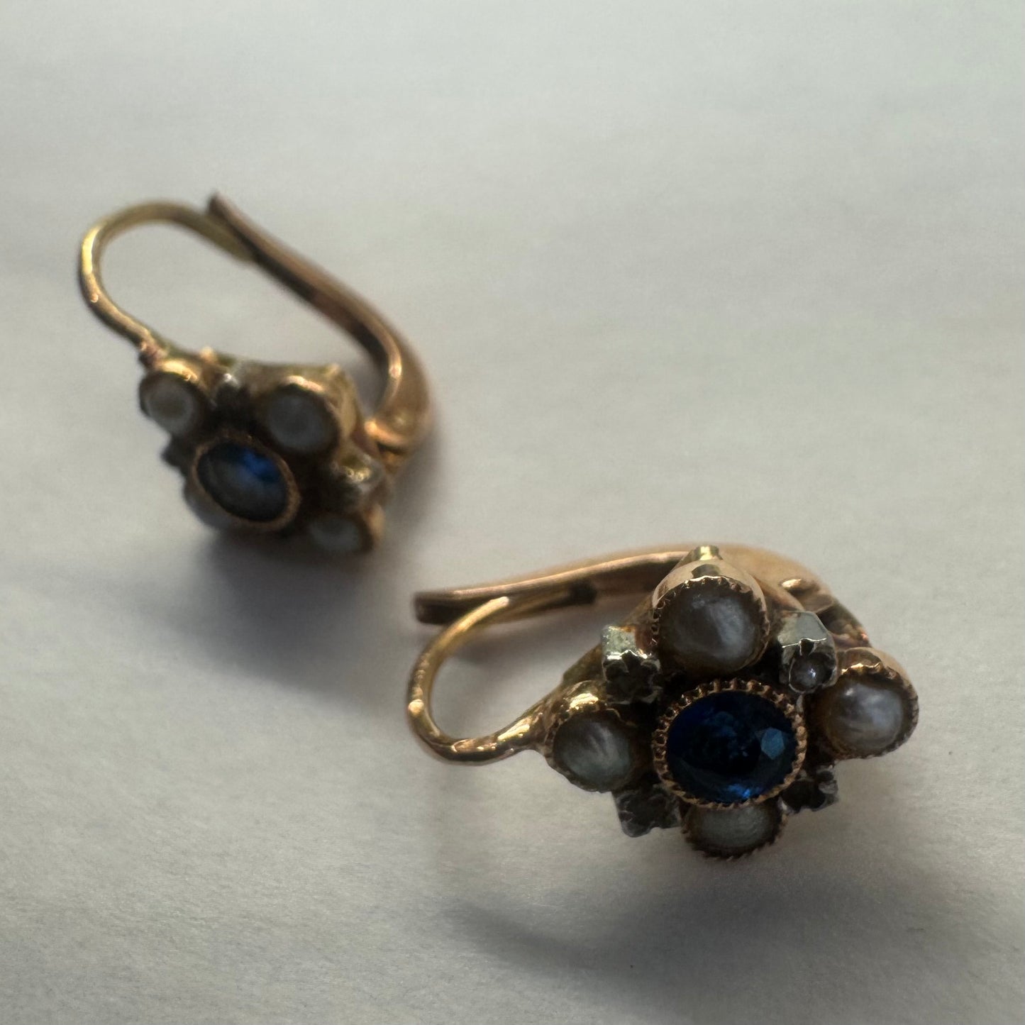 14K gold earrings featuring a round deep blue Sapphire in the center, surrounded by Pearls arranged in a floral design.