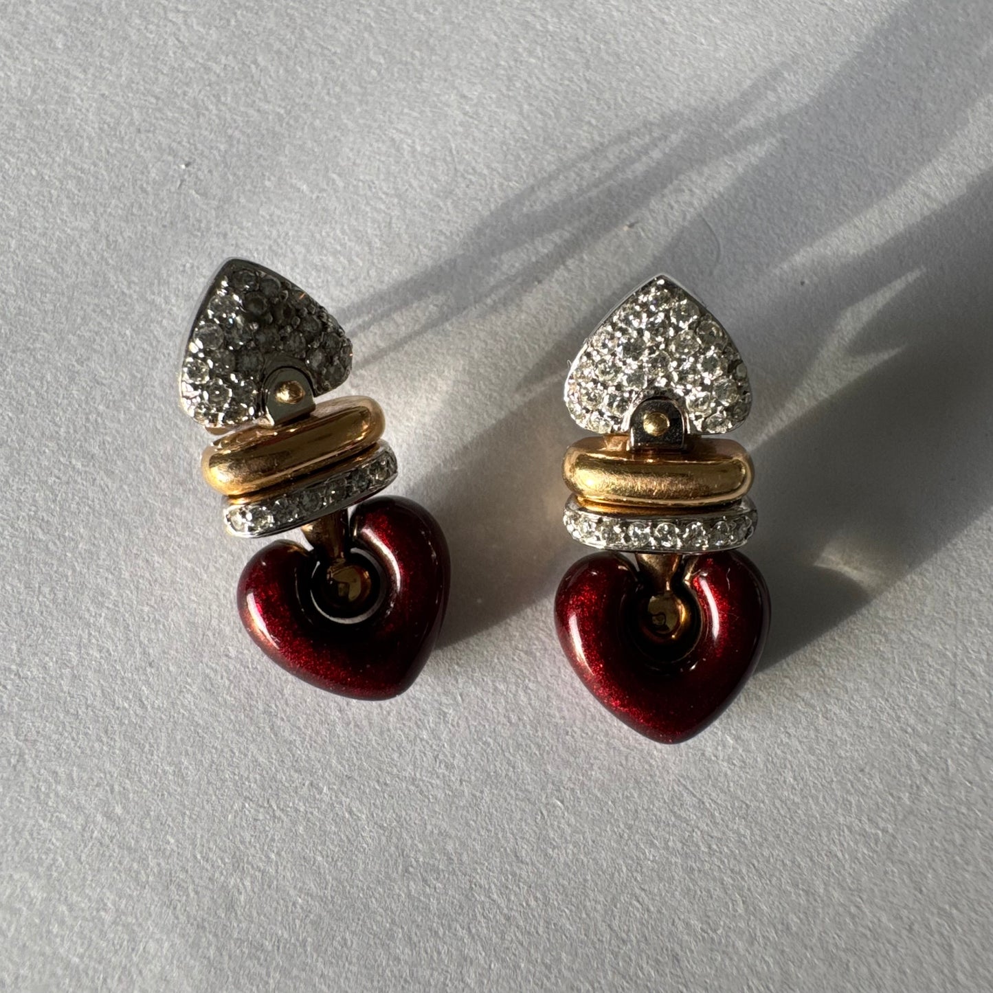 עגילי זהב 18 קראט בשילוב זהב צהוב ולבן, משובצים יהלומים בחלק העליון ובחישוק מרכזי, ובתחתית תליון לב אדום בגימור מבריק.