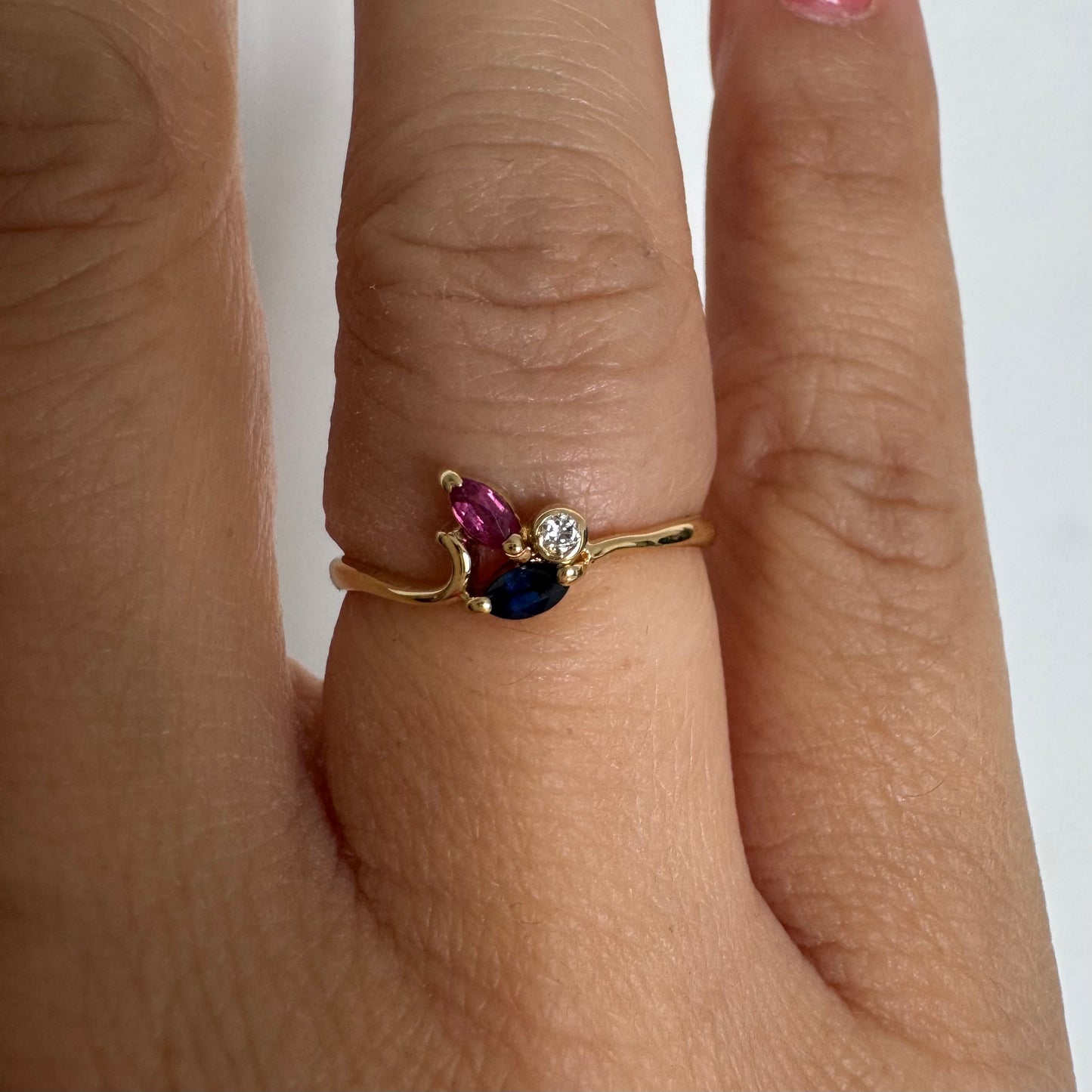 Delicate 18K gold ring set with pink and blue Sapphires alongside a sparkling center stone.