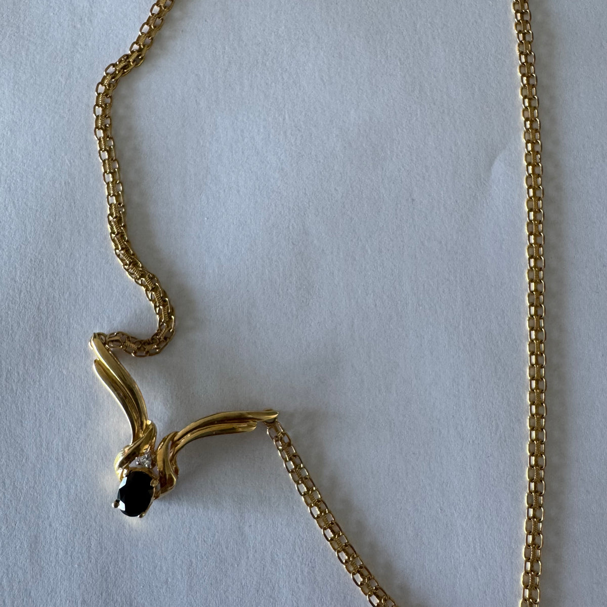 14K gold necklace featuring a flowing pendant design, set with a dark blue center Sapphire and a small Diamond above.