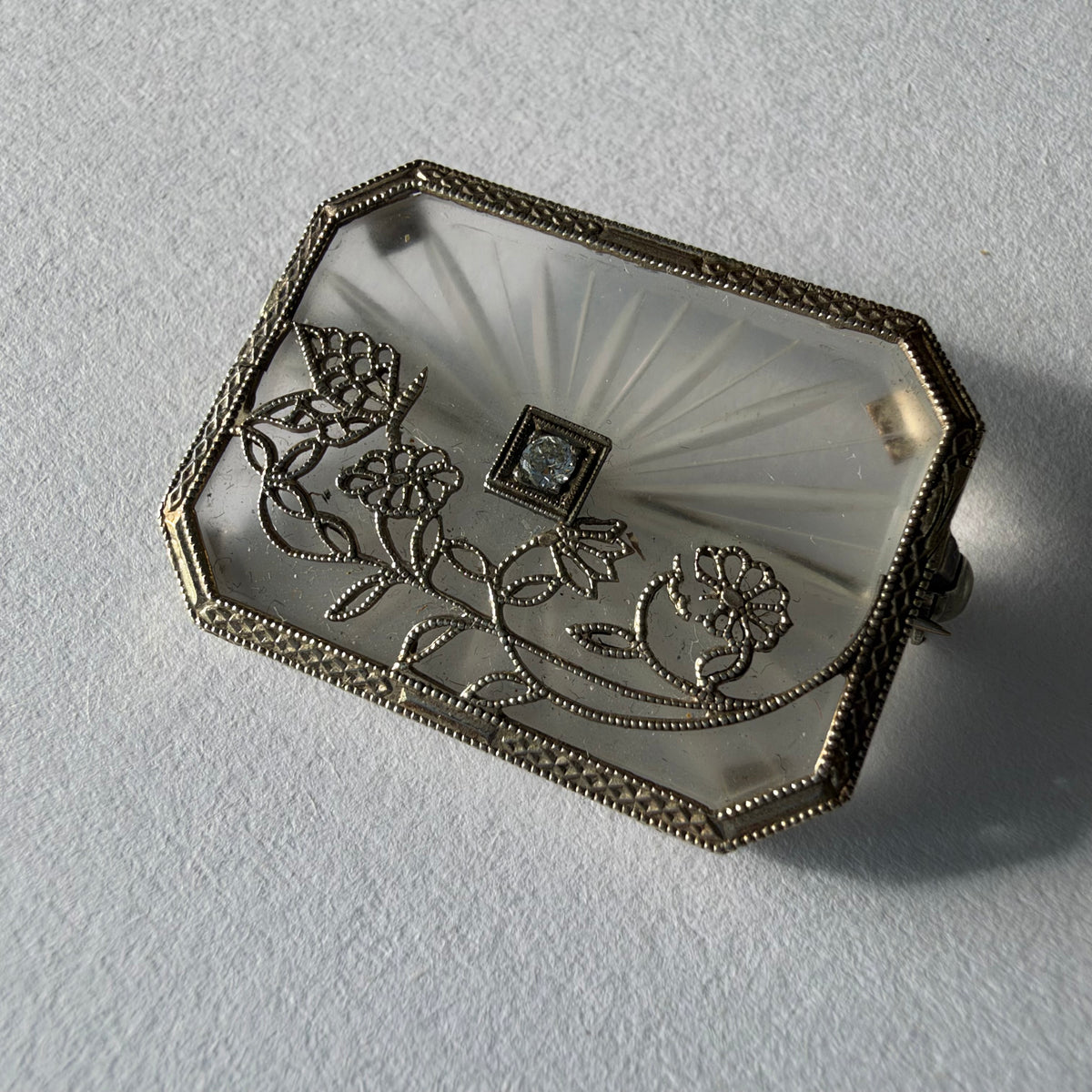 An antique Art-Deco brooch featuring a geometric design, delicate floral details & a sparkling Diamond