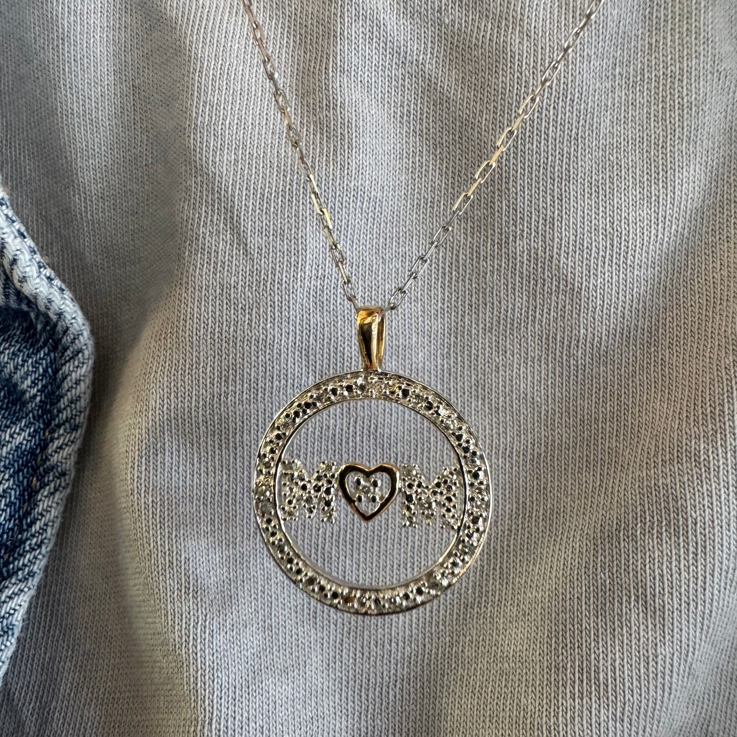 תליון זהב לבן 14 קראט עם הכיתוב ״MOM” מוקף מסגרת יהלומים עדינה.