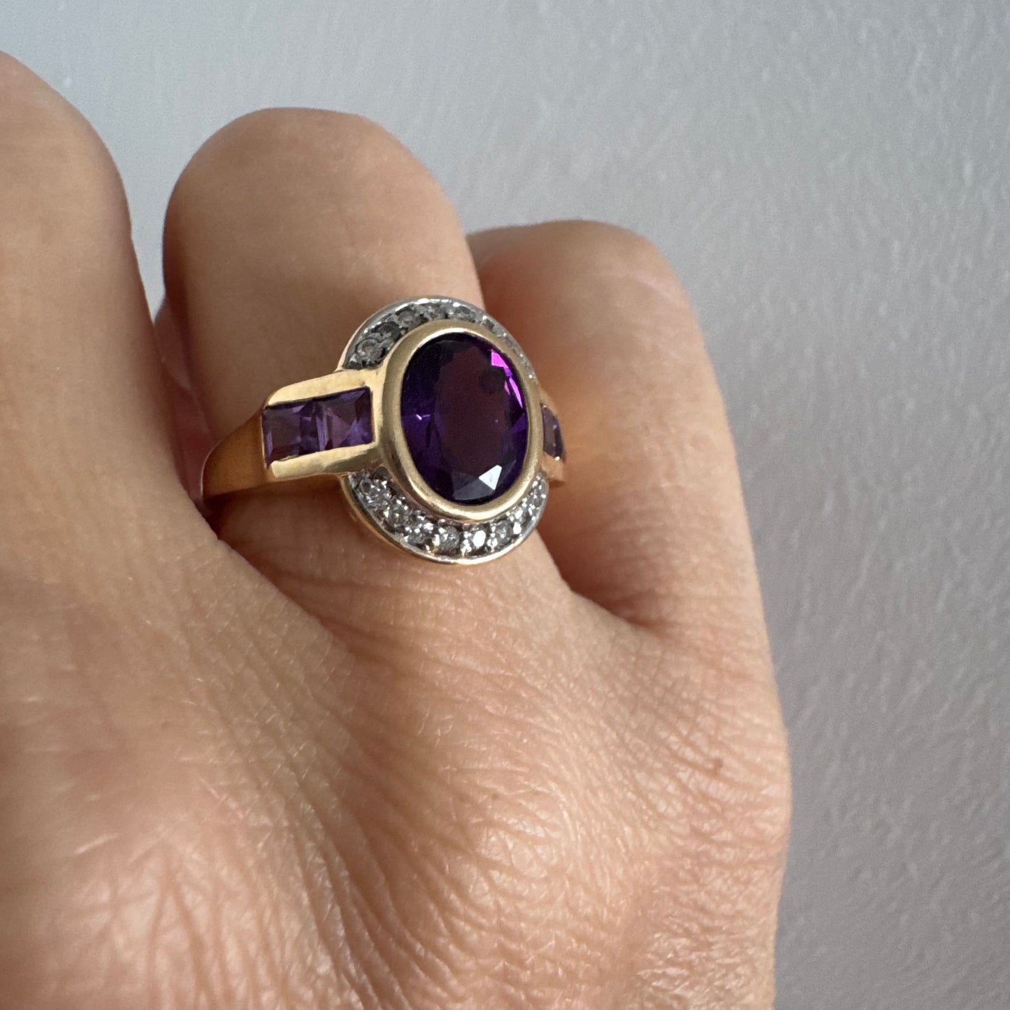 טבעת זהב 14 קראט בעיצוב ייחודי עם אבן אמטיסט אובלית מרכזית בגוון סגול עמוק, משובצת במסגרת חלקה ומודגשת ויהלומים.