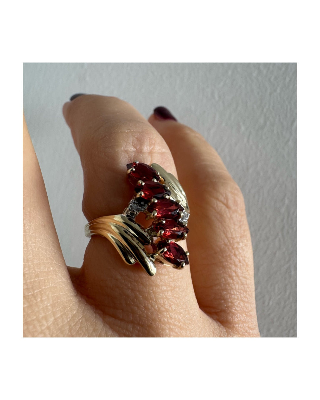 טבעת זהב צהוב 10 קראט בעיצוב דינמי ומלא תנועה, משובצת אבני גרנט בחיתוך מרקיזה בגוון אדום עמוק ובמרכזה נגיעות יהלומים לבנים.