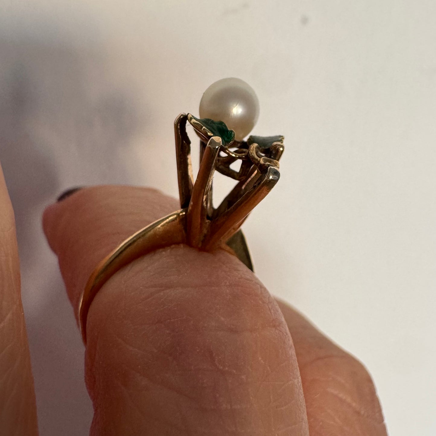 טבעת זהב 14 קראט משובצת פנינה מרכזית ומעוטרת אמייל ירוק בעבודת יד בצורת עלים.