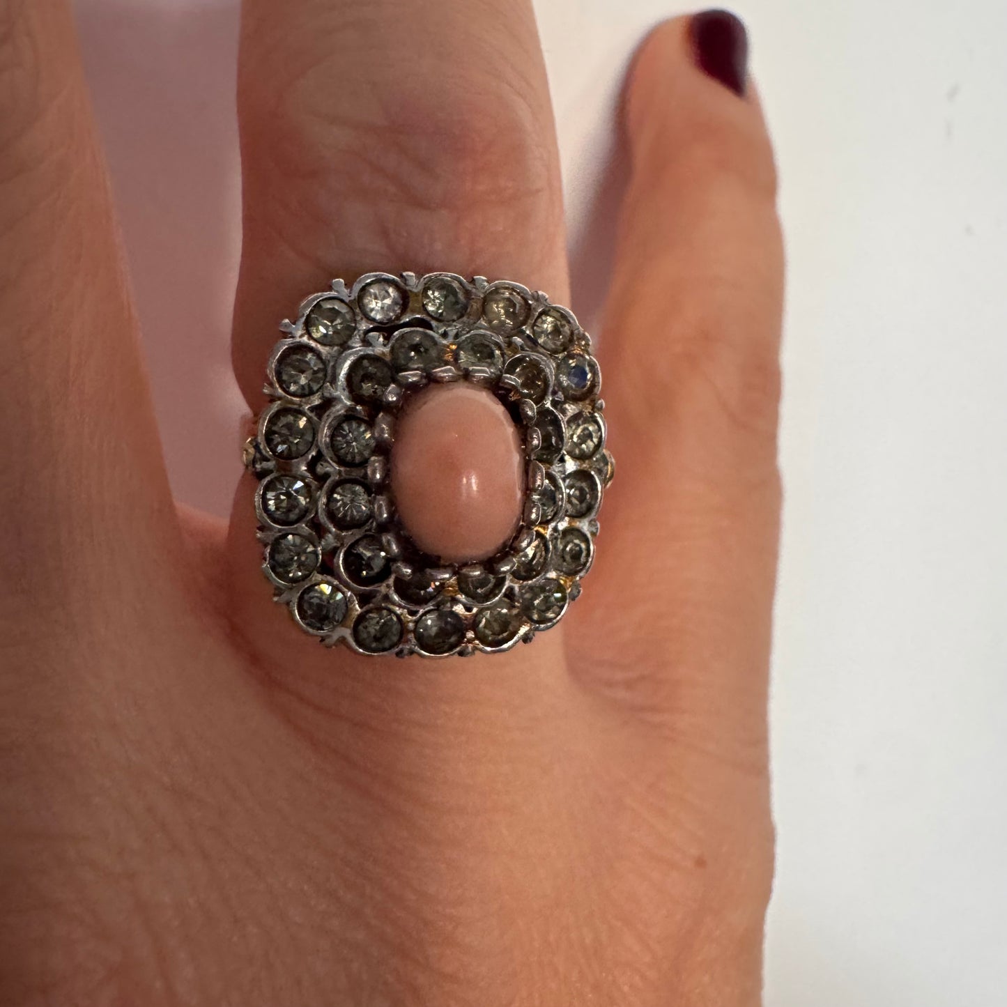 טבעת וינטג׳ עם חלק תחתון מזהב 14 קראט וחלק עליון עשוי כסף משובצת אבן קורל טבעית במרכז ומסביבה אבנים בהירות שאינן יהלומים.