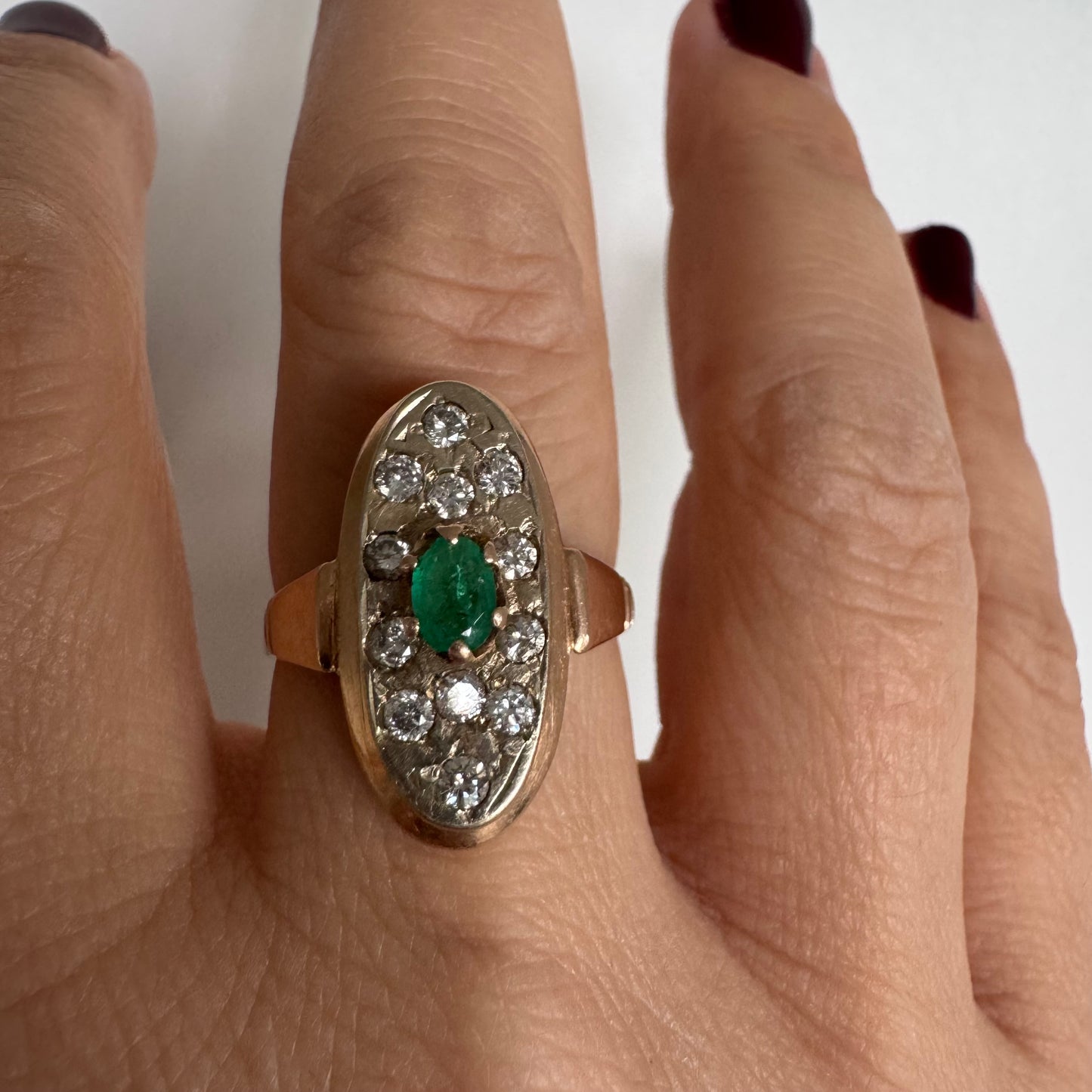טבעת זהב 14 קראט בעיצוב אלגנטי ומאורך, משובצת אבן אמרלד מרכזית ויהלומים מסביב.
