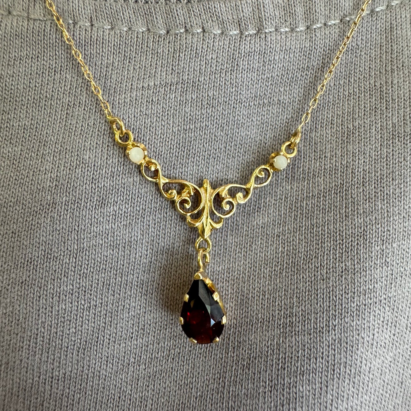 18K gold Necklace featuring an elegant scrollwork design and a striking deep-red pear-shaped Garnet drop.