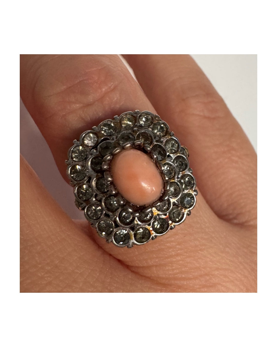 טבעת וינטג׳ עם חלק תחתון מזהב 14 קראט וחלק עליון עשוי כסף משובצת אבן קורל טבעית במרכז ומסביבה אבנים בהירות שאינן יהלומים.