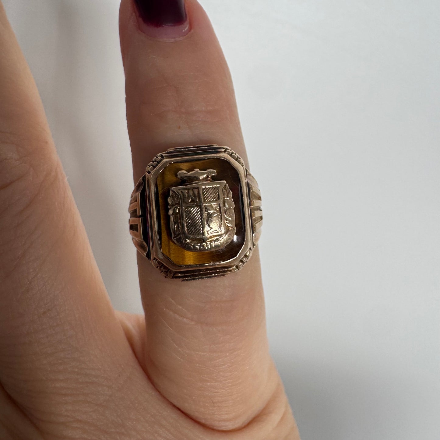 טבעת חותם זהב צהוב 10 קראט עם אבן בגוון חום-דבש ועיטור סמל מובלט במרכז.