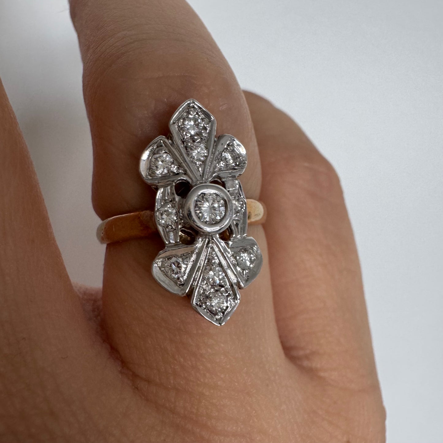 טבעת זהב לבן 14 קראט, בעיצוב אלגנטי ועדין, משובצת יהלום מרכזי עגול וסביבו יהלומים נוצצים נוספים.