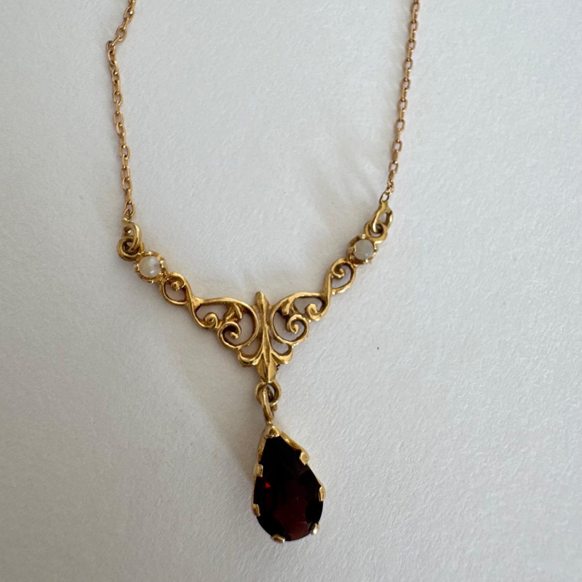 18K gold Necklace featuring an elegant scrollwork design and a striking deep-red pear-shaped Garnet drop.