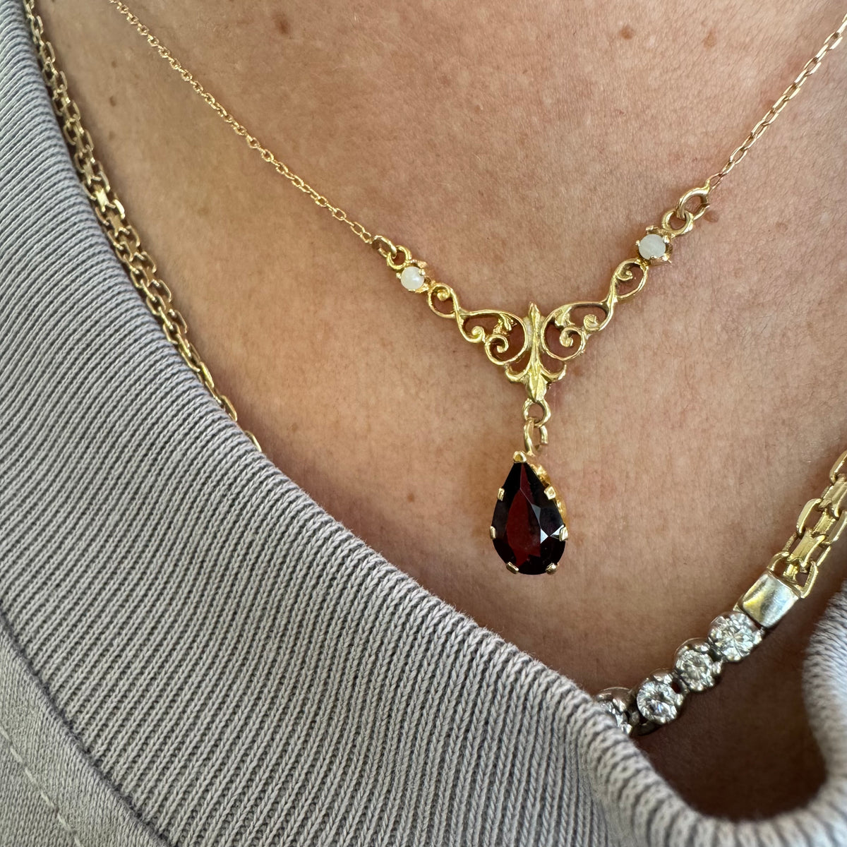 18K gold Necklace featuring an elegant scrollwork design and a striking deep-red pear-shaped Garnet drop.