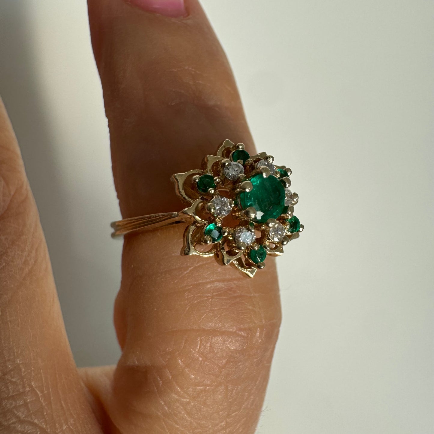 טבעת זהב 14 קראט בעיצוב פרח משובצת אבן אמרלד מרכזית, מוקפת יהלומים ואבני אמרלד נוספות