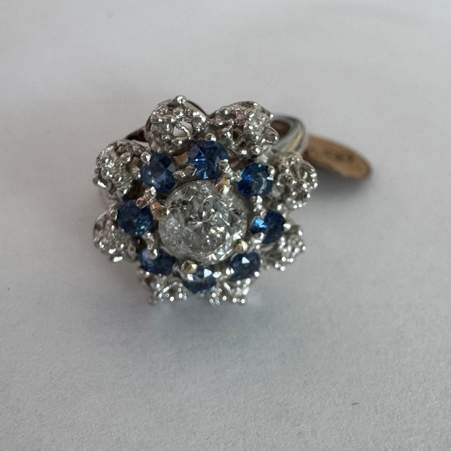 18K gold ring featuring a large round Diamond at the center, surrounded by a floral halo of purple -blue Tanzanite and & Diamonds.