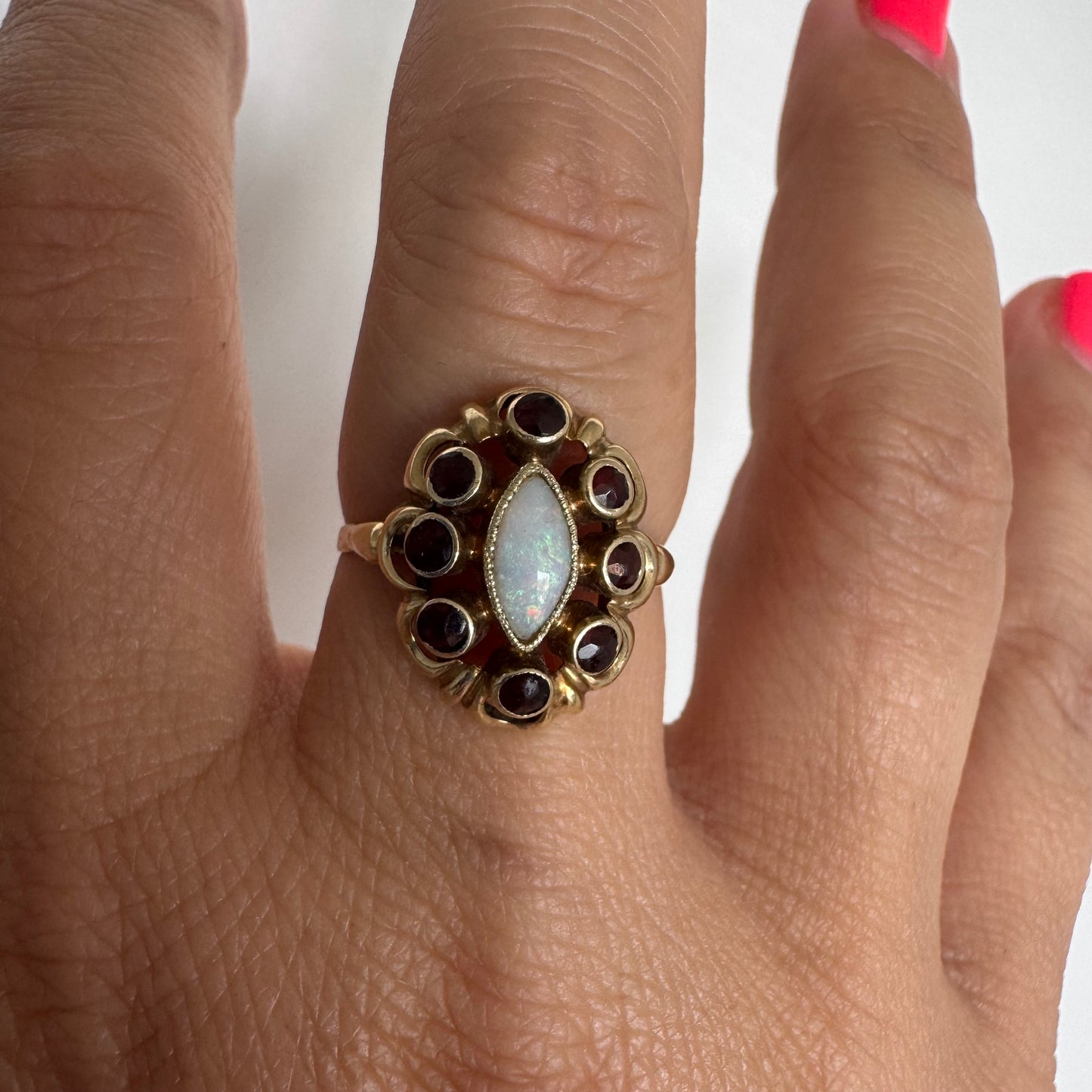 14K gold ring set with a luminous marquise-cut Opal at the center, surrounded by deep red Garnet cabochons