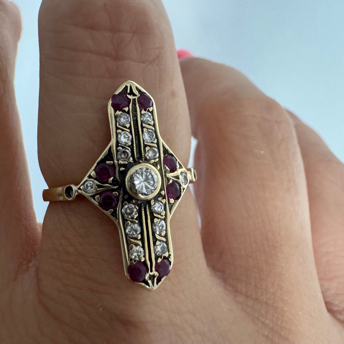 18K gold ring featuring a striking geometric design, set with a central Diamond surrounded by sparkling Diamonds and rich red Rubies.