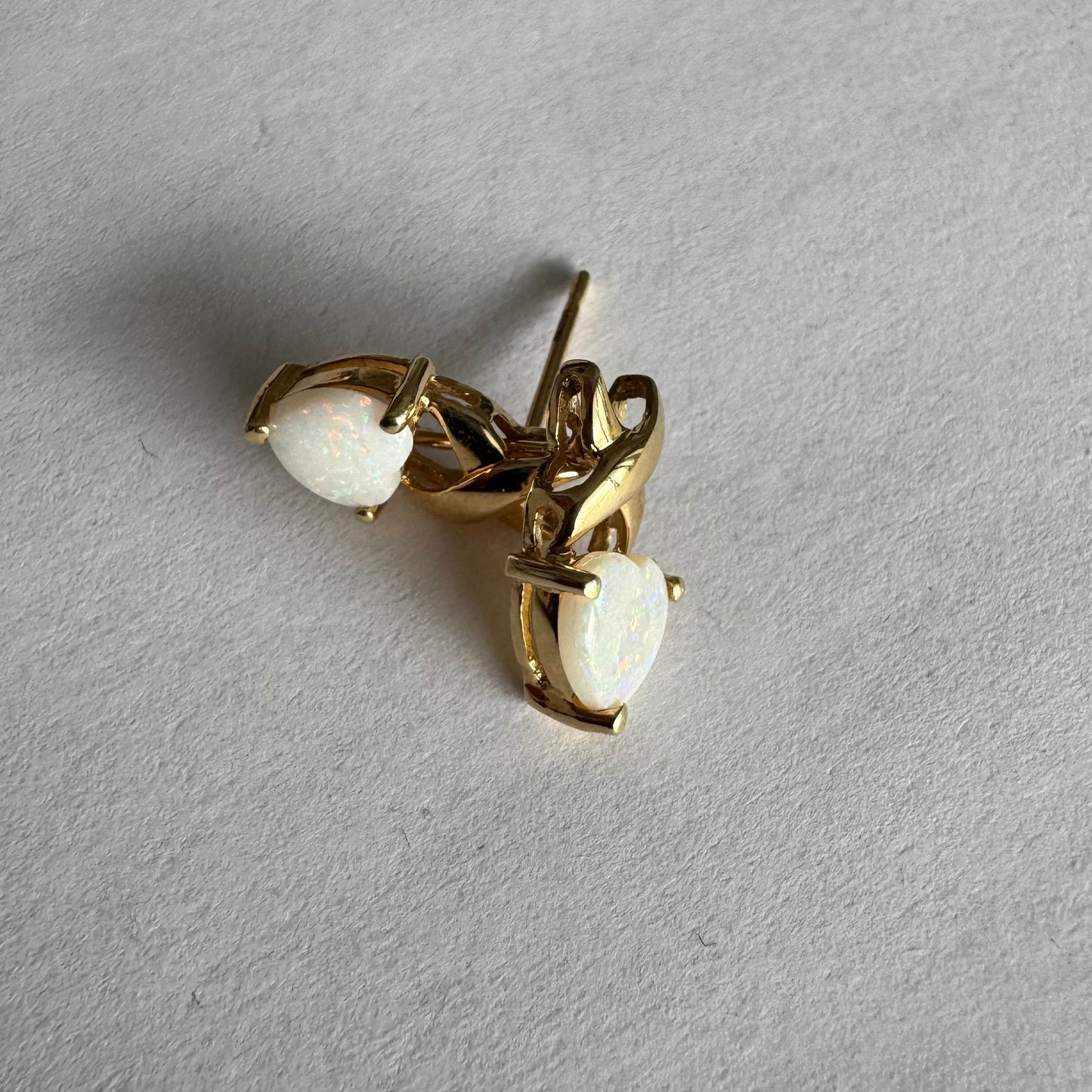 עגילי זהב צהוב 14 קראט משובצים אבני אופל בחיתוך לב, עם משחקי צבע טבעיים בגווני ירוק, ורוד וזהב.