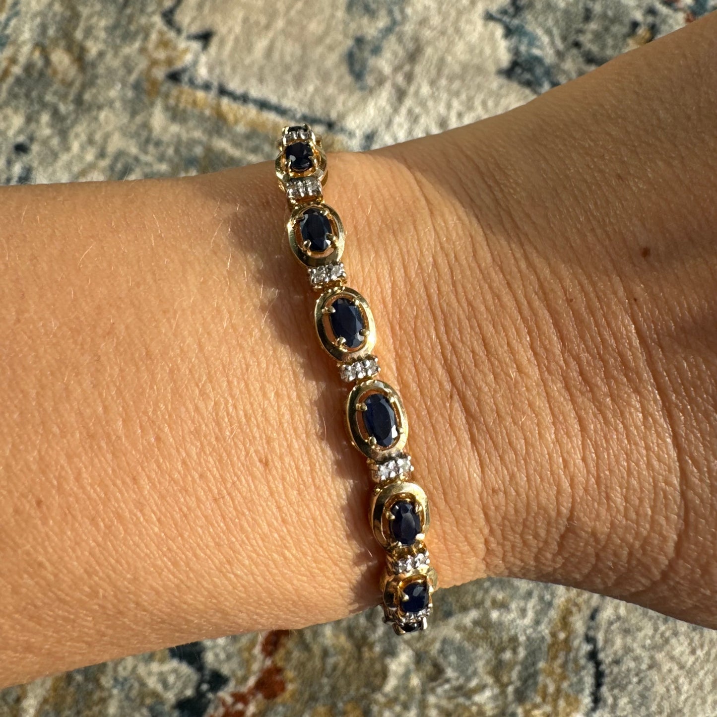 צמיד זהב צהוב 10 קראט בעיצוב קלאסי ועשיר, משובץ אבני ספיר אובליות בגוון כחול עמוק וביניהן שיבוצי יהלומים לבנים עדינים.