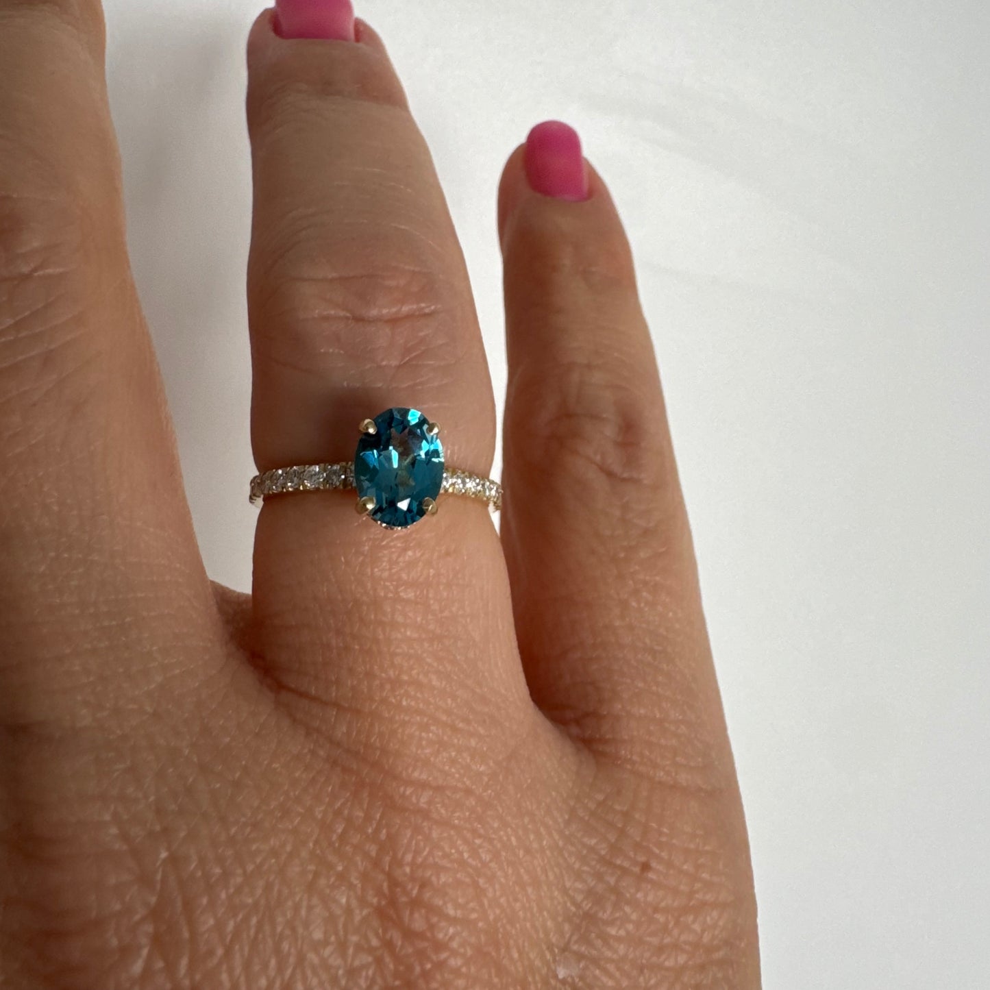 טבעת זהב צהוב 14 קראט משובצת אבן טופז כחולה אובלית בגוון טורקיז־כחול עמוק, באחיזה של ארבע שיניים עדינות ויהלומים.