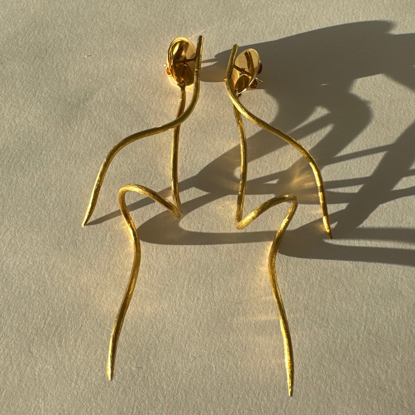 עגילי זהב צהוב 18 קראט מבית ה.שטרן, בעיצוב פיסולי וייחודי עם קווים זורמים ודינמיים.