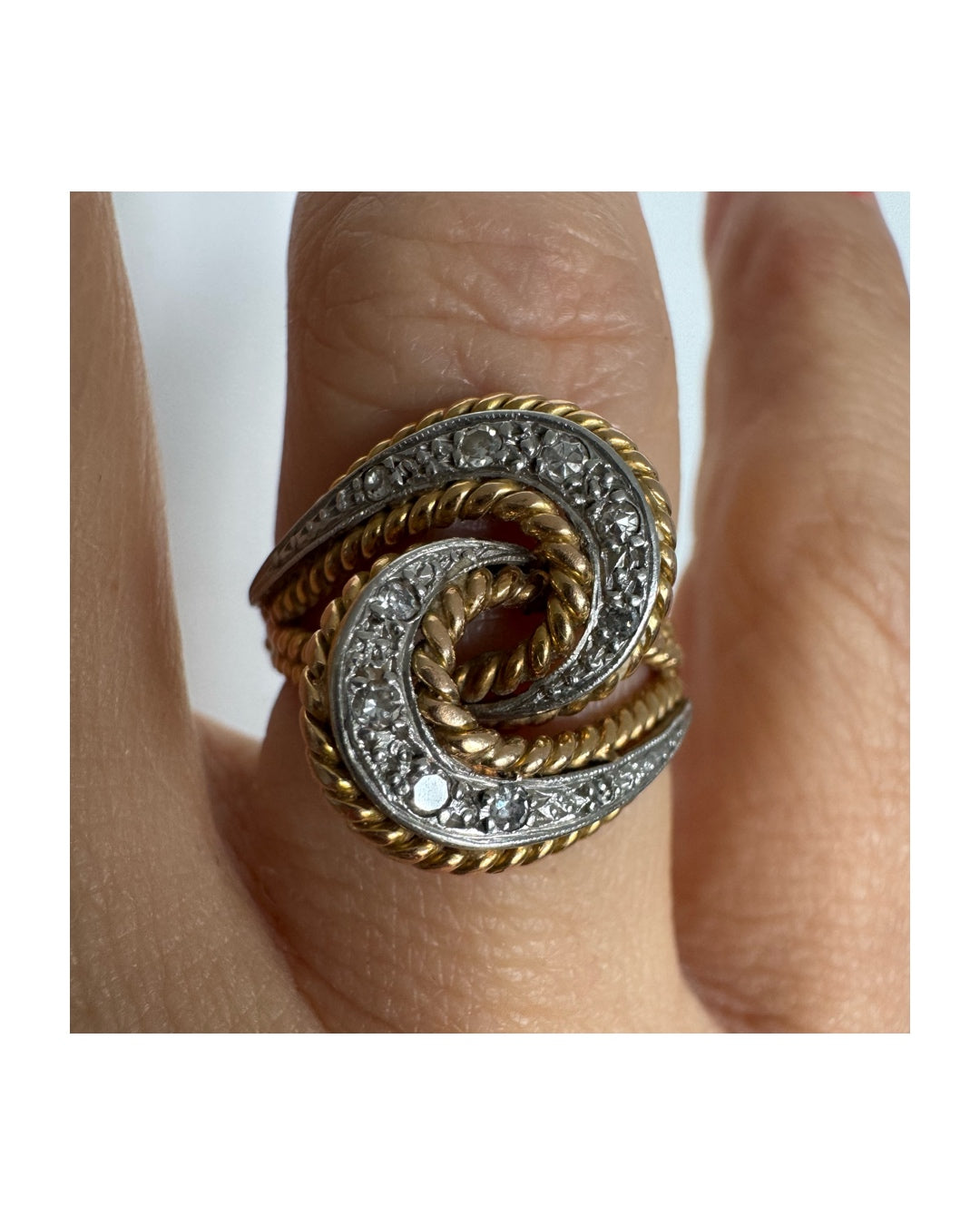 טבעת זהב 18 קראט בעיצוב ייחודי של קשרים משתלבים, המשלבת זהב צהוב וזהב לבן&nbsp;משובצת יהלומים לאורך הקימורים, היוצרים תנועה אלגנטית וברק עדין מכל זווית.