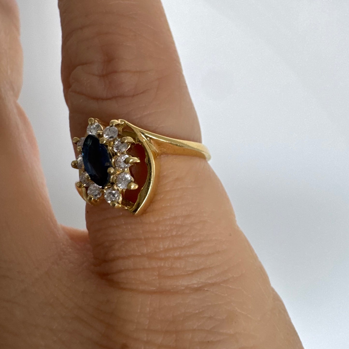 טבעת זהב צהוב 18 קראט משובצת ספיר כחול מרכזי בחיתוך מרקיזה, מוקף הילה של יהלומים המעניקים ניצוץ עדין ומדגישים את צבע האבן העמוק.