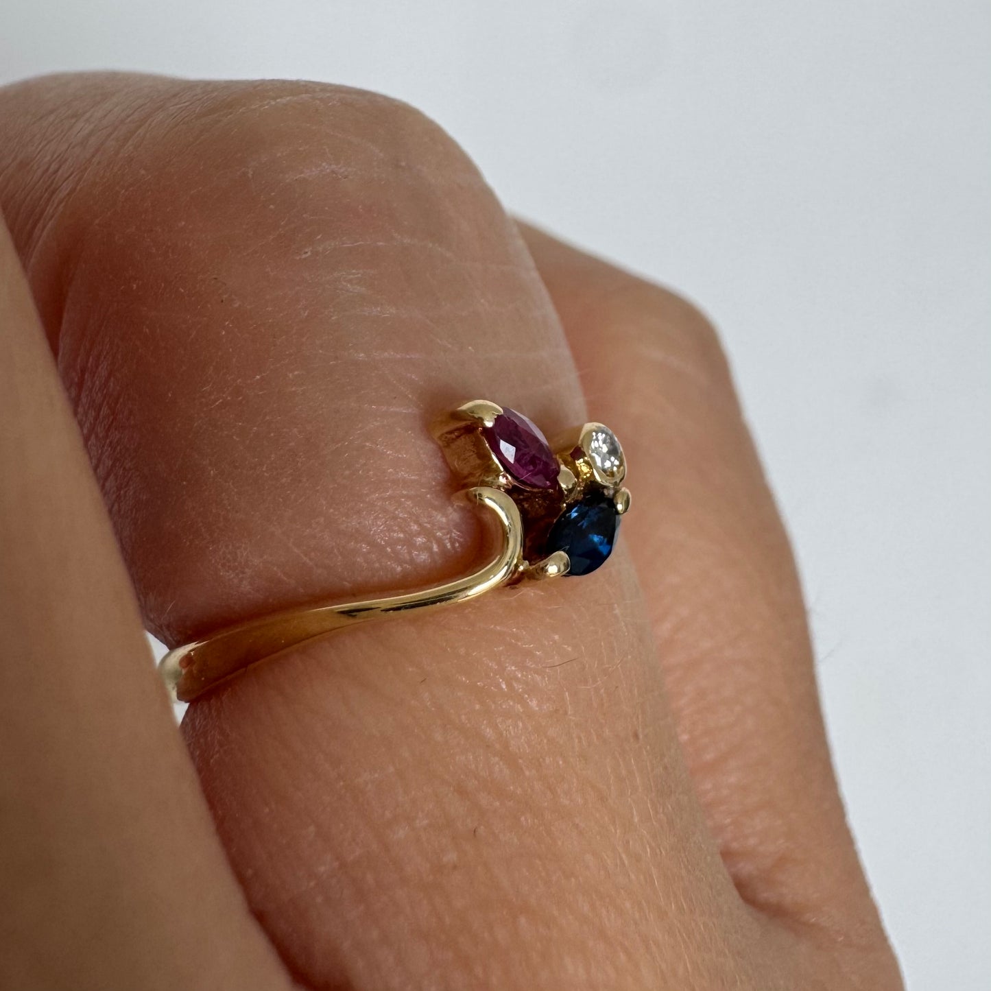 Delicate 18K gold ring set with pink and blue Sapphires alongside a sparkling center stone.