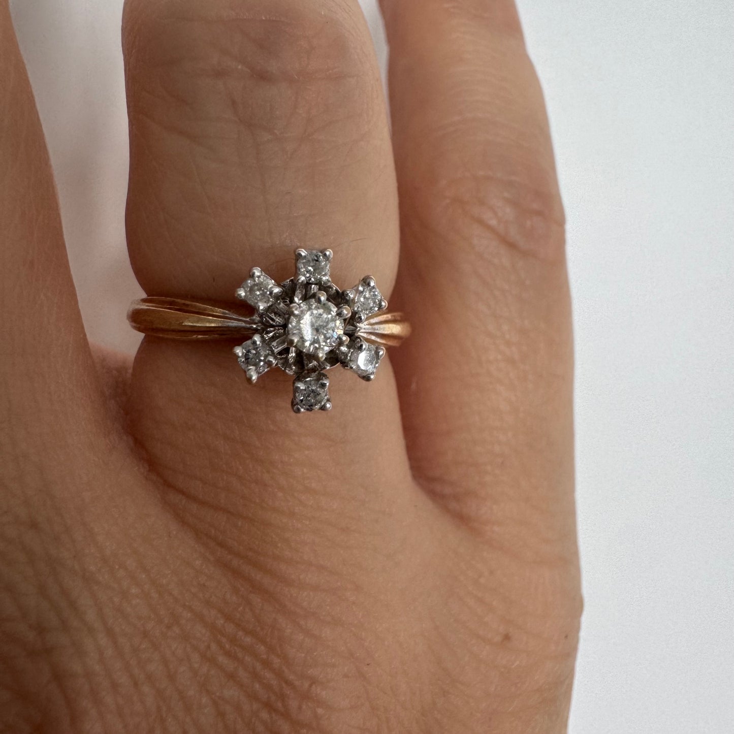 טבעת זהב 9 קראט משובצת יהלום מרכזי ויהלומים מסביב בעיצוב פרח קלאסי.