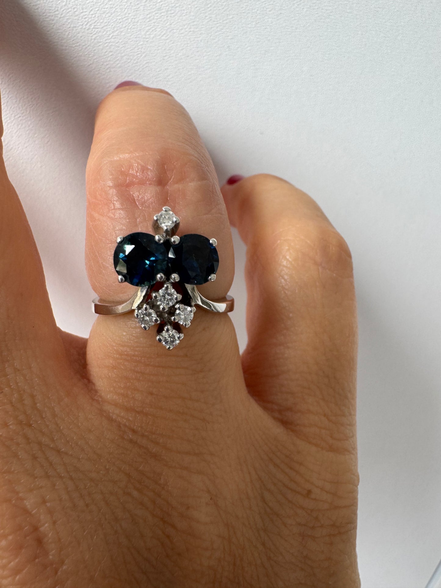 14K gold ring set with two deep blue oval Sapphires accented by clusters of brilliant white Diamonds.