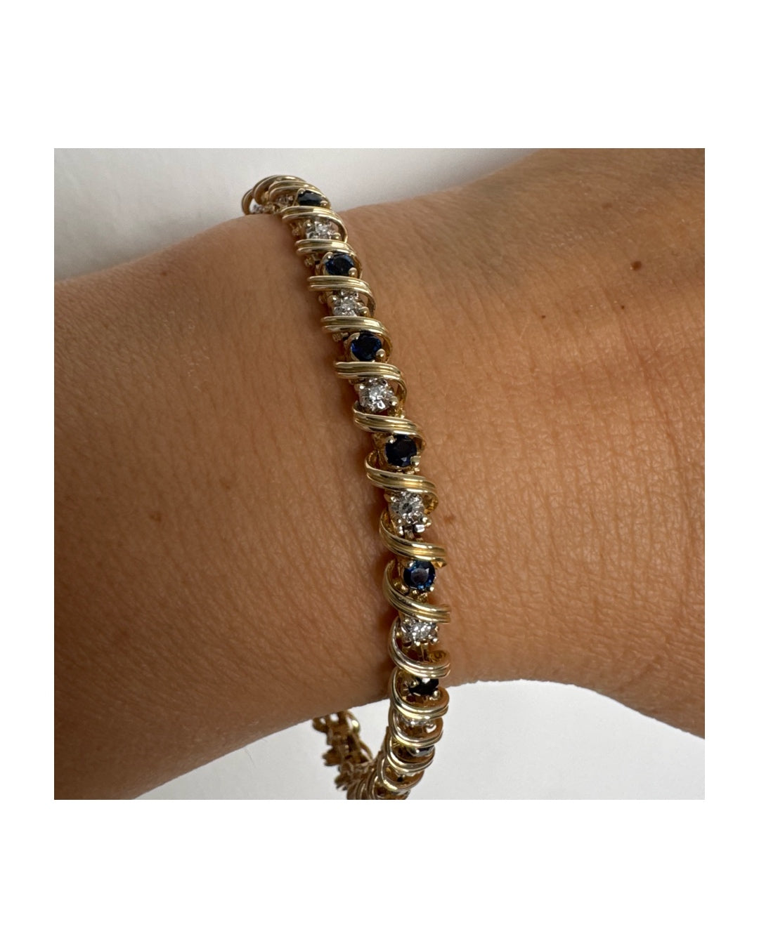 צמיד זהב צהוב 14 קראט משובץ אבני ספיר כחולות ויהלומים, המשובצים בעיצוב זורם עם קווים מעוגלים העוטפים כל אבן.