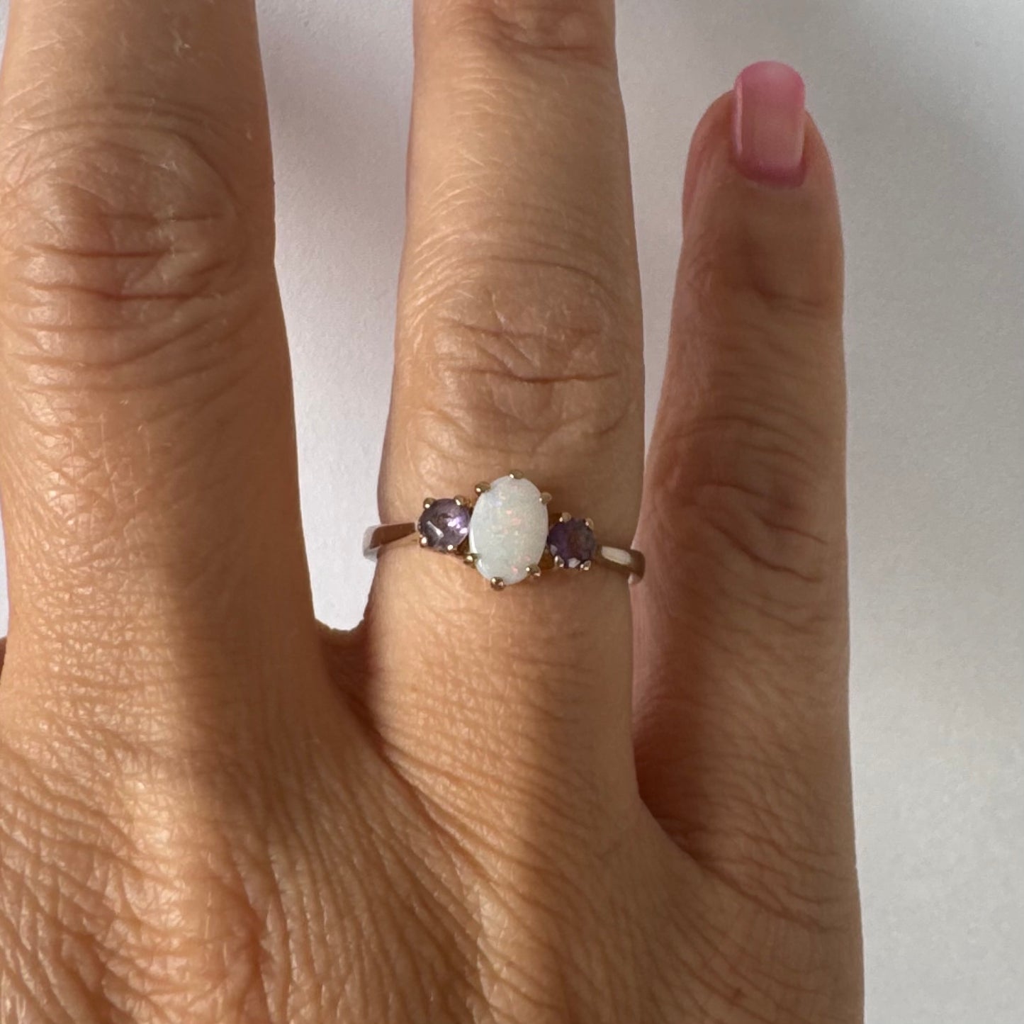 9K gold ring set with an oval Opal at the center, flanked by two delicate purple stones.