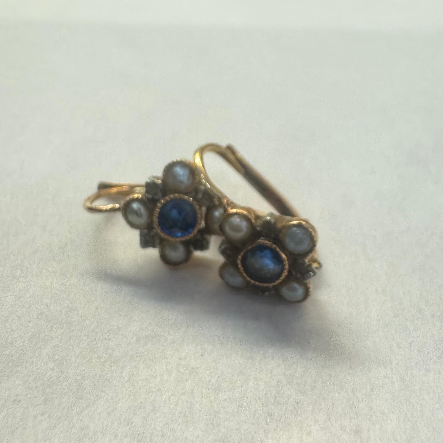 14K gold earrings featuring a round deep blue Sapphire in the center, surrounded by Pearls arranged in a floral design.