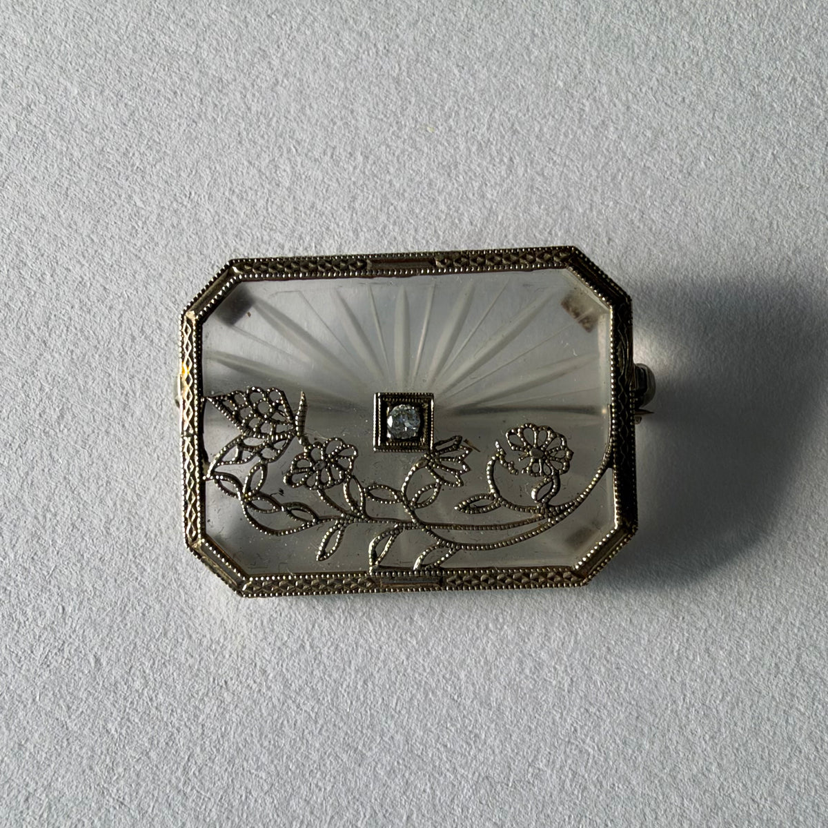 An antique Art-Deco brooch featuring a geometric design, delicate floral details & a sparkling Diamond