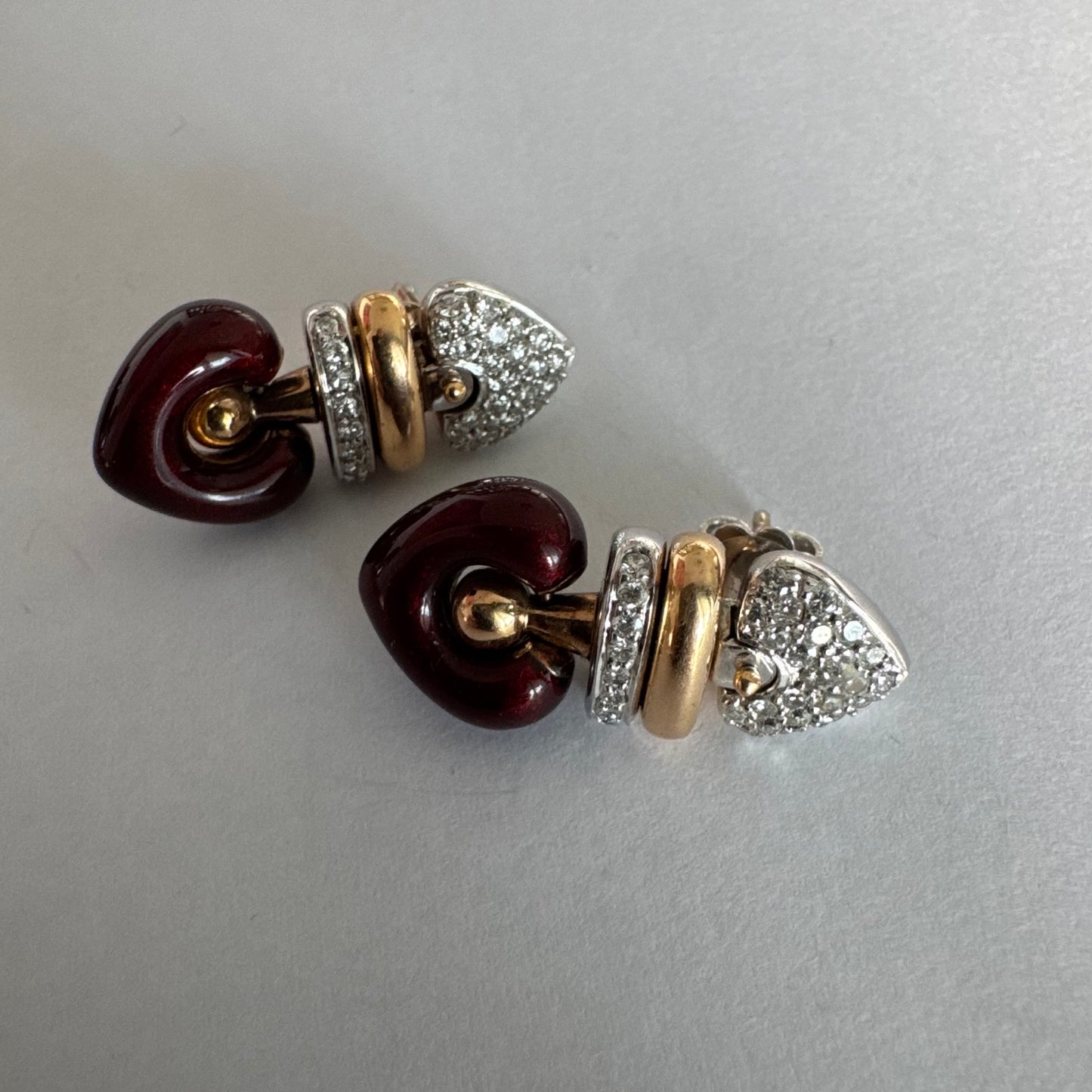 עגילי זהב 18 קראט בשילוב זהב צהוב ולבן, משובצים יהלומים בחלק העליון ובחישוק מרכזי, ובתחתית תליון לב אדום בגימור מבריק.