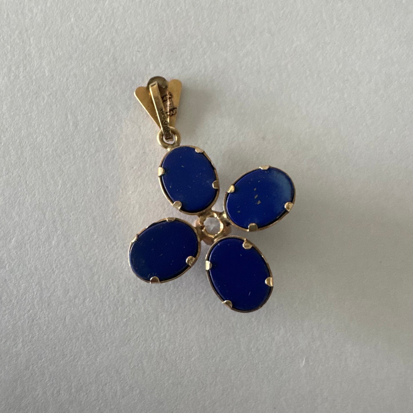 תליון זהב צהוב 14 קראט בעיצוב פרח סימטרי, משובץ ארבע אבני לפיס לזולי בגימור קבושון אובלי ובמרכזן יהלום עגול בוהק.