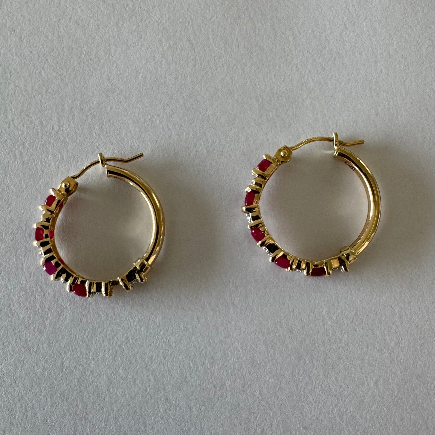 עגילי חישוק זהב צהוב 14 קראט משובצים אבני רובי בגוון אדום עמוק, בשילוב יהלומים המעניקים ברק עדין בין האבנים.
