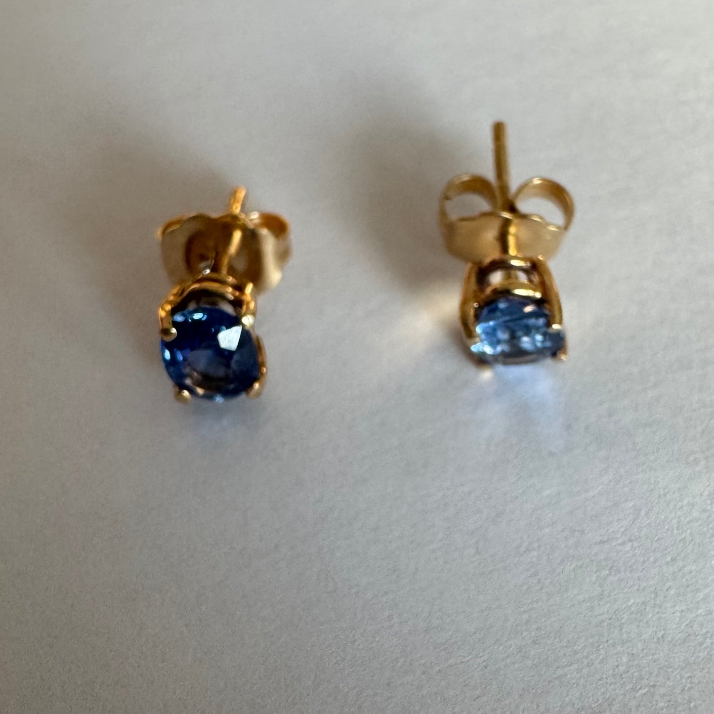 עגילי זהב 14 קראט קטנים צמודים לאוזן משובצים אבני טנזנייט בחיתוך אובלי, בגוון כחול־סגלגל עמוק ומעודן.