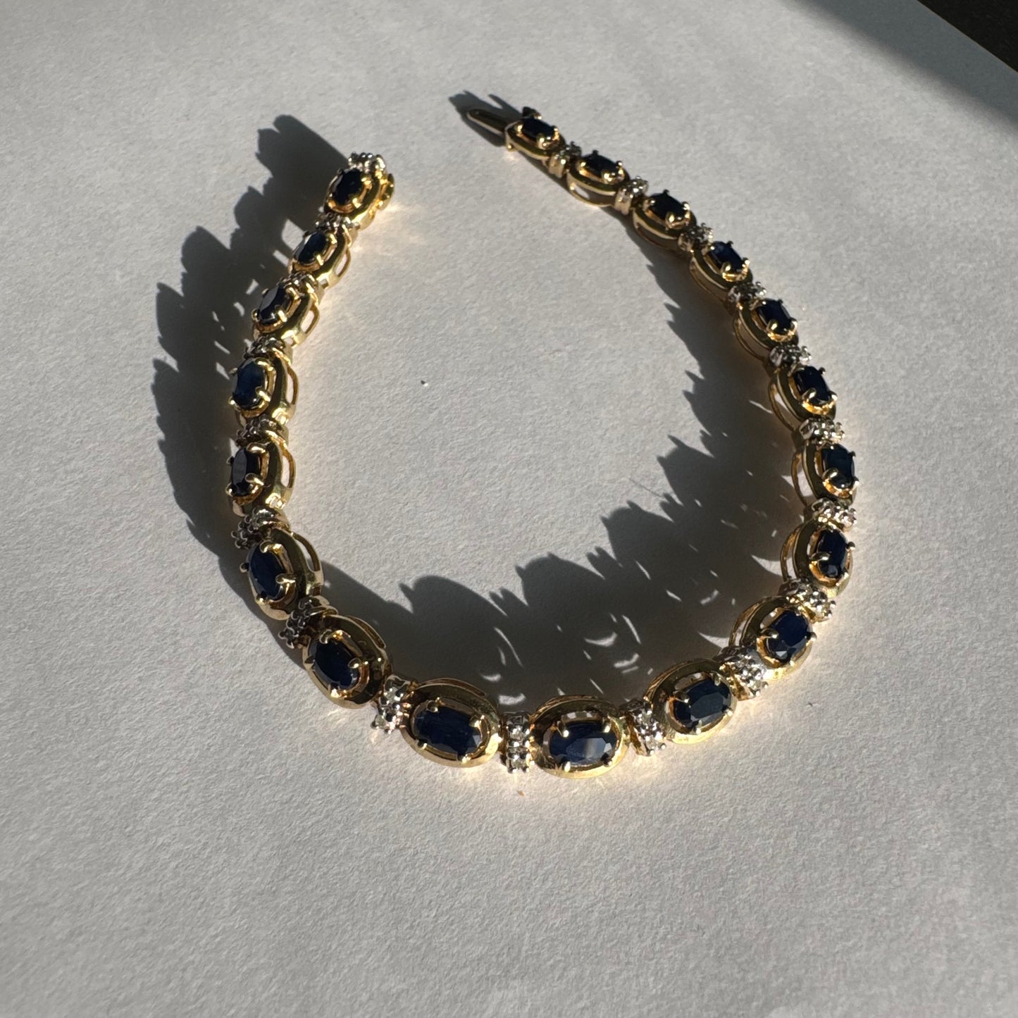 צמיד זהב צהוב 10 קראט בעיצוב קלאסי ועשיר, משובץ אבני ספיר אובליות בגוון כחול עמוק וביניהן שיבוצי יהלומים לבנים עדינים.