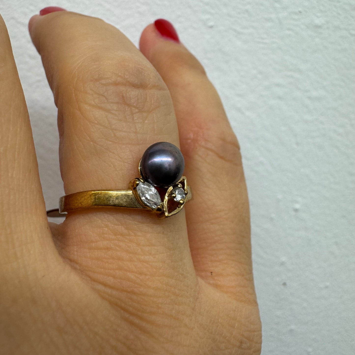 14K gold ring set with a Black Pearl at the center and clear gemstones on the sides.