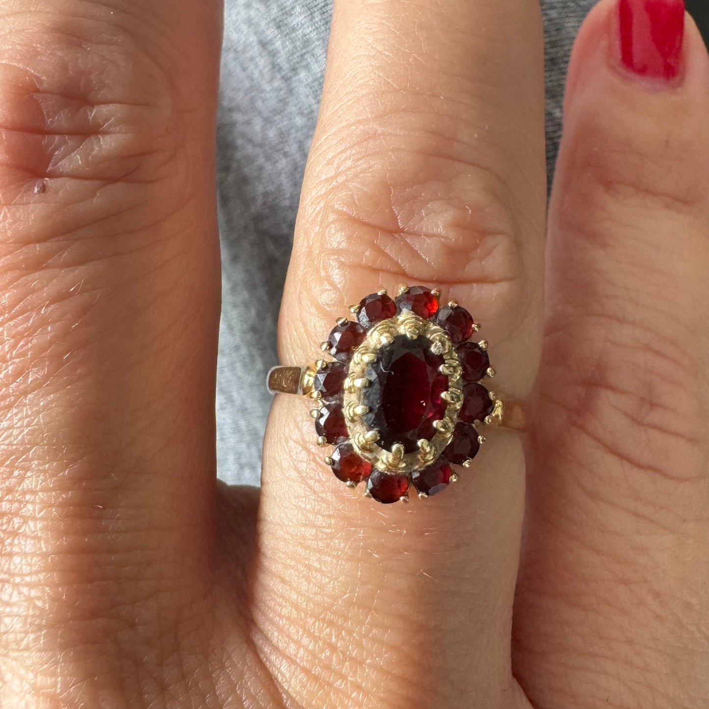 טבעת זהב צהוב 18 קראט משובצת אבן גרנט אובלית במרכז, מוקפת באבני גרנט קטנות בסידור אליפטי קלאסי.