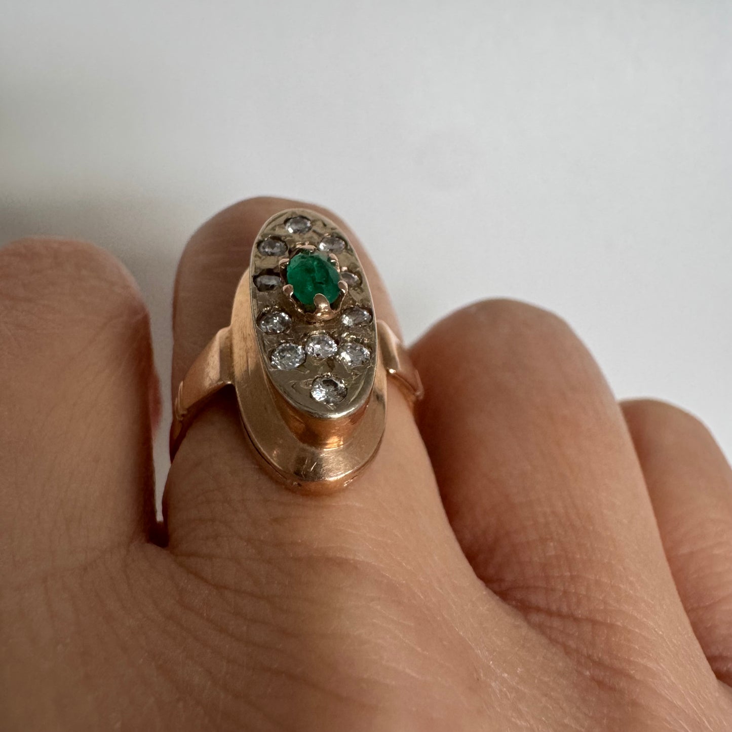 טבעת זהב 14 קראט בעיצוב אלגנטי ומאורך, משובצת אבן אמרלד מרכזית ויהלומים מסביב.