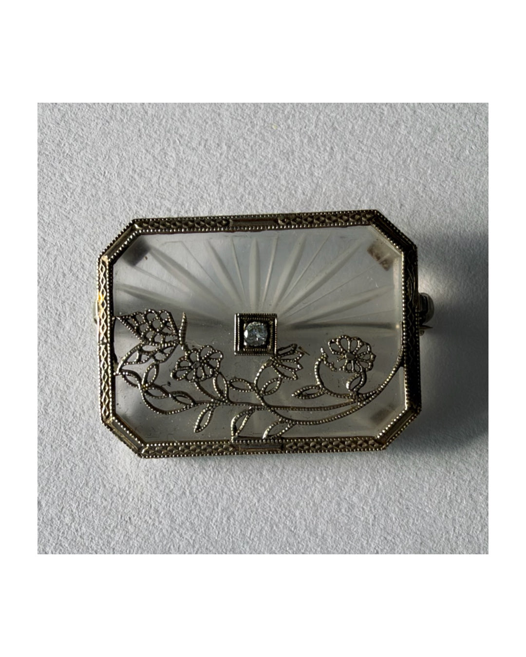 An antique Art-Deco brooch featuring a geometric design, delicate floral details & a sparkling Diamond