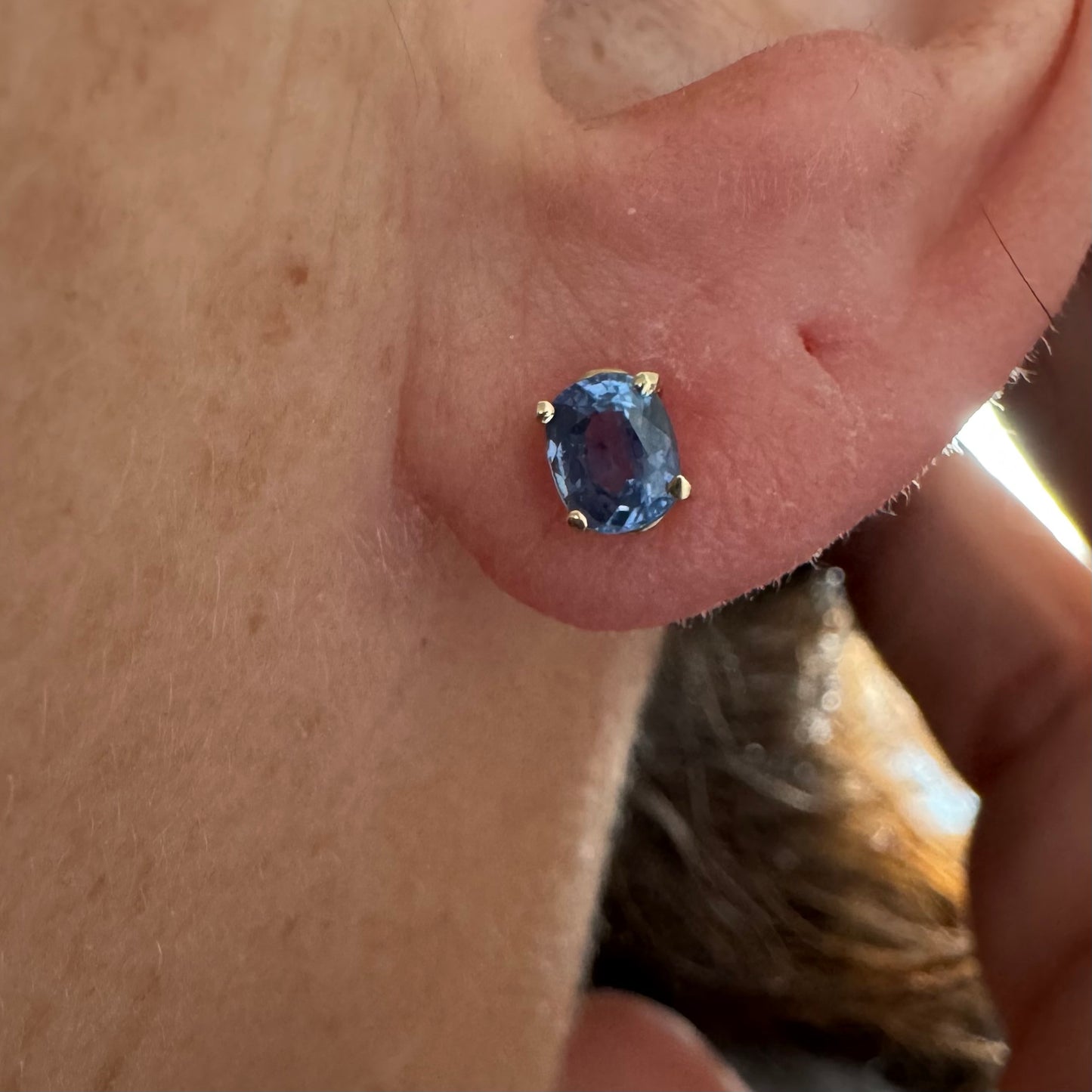 עגילי זהב 14 קראט קטנים צמודים לאוזן משובצים אבני טנזנייט בחיתוך אובלי, בגוון כחול־סגלגל עמוק ומעודן.